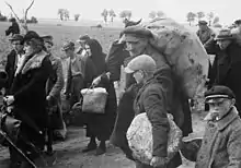 Photographie en noir et blanc d'hommes, femmes et enfants portant quelques colis et marchant dans la même direction.