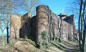 Ruines d'un château-fort massif flanqué de plusieurs tours et entouré d'arbres.