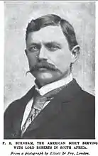 Photographie d'un homme d'age mur l'air dur en costume sombre avec une moustache en guidon.