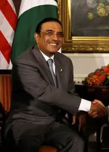 Phptp montrant un homme souriant assis en costume serrant la main d'une autre personne