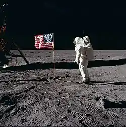 Photographie en couleur de Buzz Aldrin près du drapeau américain planté sur la Lune.