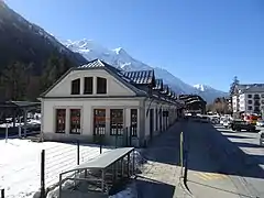 Vue de côté du bâtiment voyageurs depuis l'escalier menant à la passerelle surplombant les voies de la gare.