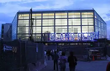 The Whitehall Terminal is housed in a glass building with a blue "Staten Island Ferry" marquee over the entrance.