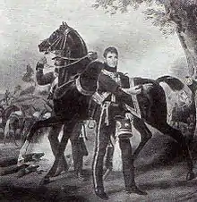 Portrait en pied d'un colonel de cavalerie français, tenant sa coiffure de la main gauche. Derrière lui, l'un de ses cavaliers tient son cheval par la bride.