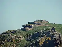 Photographie en couleur d'un bunker à trois étages en escalier, construit contre une colline sur une position surélevée, en direction de la gauche.