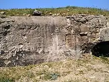 Mur d'un blockhaus éclaté en plusieurs endroits (impacts d'obus visibles). Herbe sur le dessus.