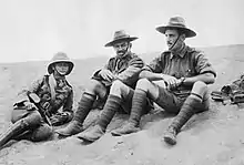 Portrait en noir et blanc de trois hommes en uniforme militaire, assis par terre.