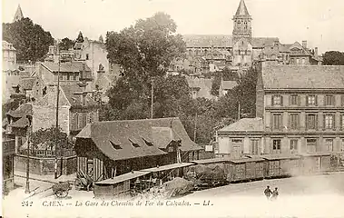 Les wagons au premier plan sont des wagons plats et des couverts de 10 tonnes à deux essieux. Au second plan, devant la gare, se trouvent une baladeuse-mixte-fourgon et une baladeuse ouverte.