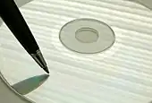 Photographie d'un stylo tenu au-dessus d'un CD, comme pour écrire quelque chose sur le plastique.