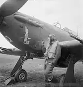 Photo noir et blanc d'un homme en combinaison de vol, adossé à l'aile d'un avion