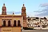 Au premier plan, sur la moitié gauche de la photographie, une partie de la façade du museo del Planchado ; en arrière-plan, sur la moitié droite, panorama d'habitations de Zacatecas.