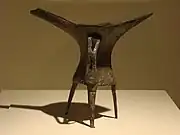 L'évolution des matières et des décors sur une même forme, le tripode jue, au cours de l'âge du Bronze ancien ; de gauche à droite : exemplaires en céramique et en bronze de la période d'Erlitou sans décor, et exemplaire en bronze de la période d'Erligang décoré d'un taotie.