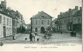 Les anciennes halles, construites en 1850 par Firmin Lombard, étaient sous la mairie.La vue est prise depuis l'autre bout de la place, en contrebas de la motte féodale.