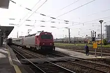 Un train de voyageurs est en gare. On peut voir au loin les voies de garage pour les trains de marchandises.