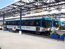 Vue de deux bus en gare routière sous une structure métallique avec le quai en premier plan.