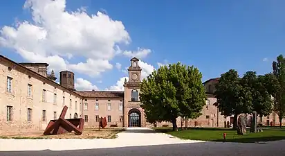 Vaste cour dominée par un portail monumental surmonté d'un clocheton. En arrière-plan à gauche, la tour-lanterne de l'église.