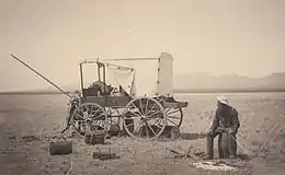 Un cow boy assis devant son chariot dans la grande plaine. Il se photographie lui-même en actionnant un cordon qui déclenche la prise de vue.