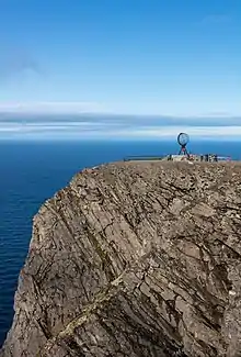 Un arrondi rocailleux plonge dans la mer. Un aménagement à touristes sur le plateau.