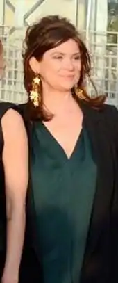 Portrait d'une femme vêtue d'une robe vert foncé, arborant un léger sourire et portant des boucles d'oreille dorées.