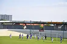 Joueurs se disputant le ballon de la tête devant un but. Au fond, les tribunes sont vides.