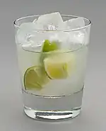 Un verre d'alcool avec des glaçons et des morceaux de citrons verts dedans