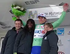 De trois-quarts, quatre personnes sourient. Un coureur au maillot vert serre les poings et lève les bras au ciel.