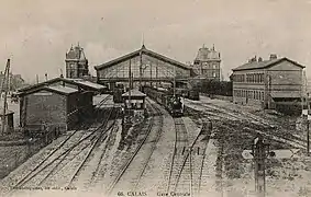 Vue des voies et des quais. Les bâtiments voyageurs sont visibles de part et d'autre de la halle métallique.