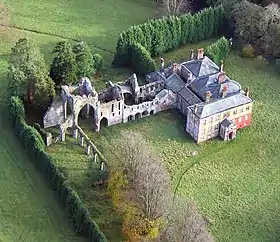 Photographie aérienne d'un manoir jouxtant des ruines d'église, dans un paysage boisé