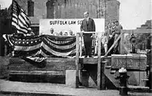 Coolidge se tient sur une estrade décorée par des drapeaux américains.