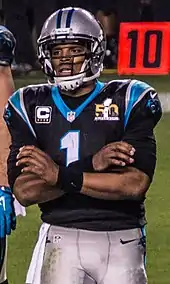 Cam Newton croisant les bras dans un maillot noir des Panthers ayant le logo du Super Bowl 50.