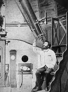 Photographie en noir et blanc d'un homme barbu utilisant un instrument astronomique.