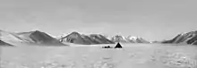 Photo en noir et blanc d'une tente pointue isolée sur un glacier dans une vaste vallée.
