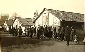 Photo noir et blanc de quelques dizaines de personnes, y compris des enfants, devant des baraquements