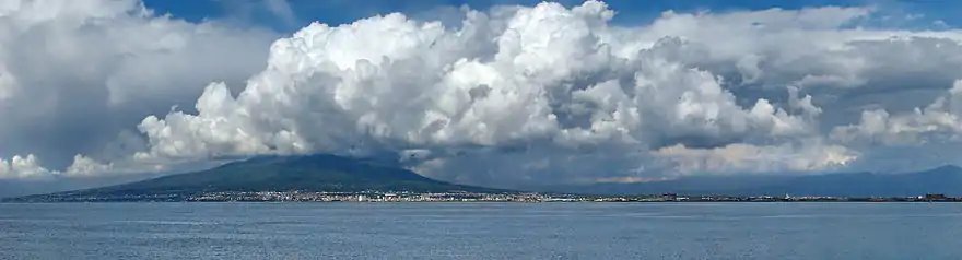 Baie de Naples, Vésuve au loin, nuages blancs dans ciel bleu.