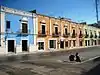 Une rue dans la ville de Campeche. Des maisons de même hauteur mais de couleurs différentes sont alignées en arrière-plan. En bas à droite de l'image est garé un scooter.