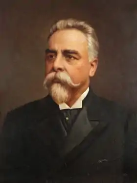 Portrait en buste d'un homme aux cheveux blancs, portant moustache et barbiche, vêtu d'un costume sombre et regardant vers sa droite d'un air grave.