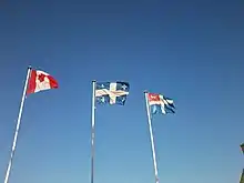 Drapeaux du Canada, du Québec et de Saint-Malo flottant au vent, par temps clair.