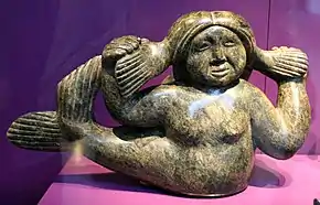 Sculpture de femme avec queue de poisson, tenant ses nattes dans les deux mains.