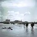 Soldats de l'infanterie canadienne débarquant le 6 juin 1944 sur la plage de Juno Beach et se dirigeant vers Bernières-sur-Mer, que l'on aperçoit en  arrière-plan.