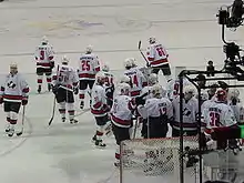 Photographie d'une équipe de hockeyeurs en maillot blanc et rouge sur une patinoire.