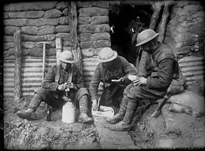 Photographie en noir et blanc de soldats assis dans une tranchée en train de manger
