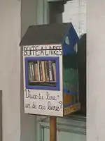 Photographie en couleurs d'un casier vitré rempli de livres, en bord de rue.