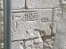 Photographie en couleur d'un pierre de taille gravée avec des repères et des dates.