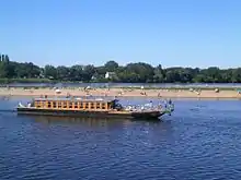 Photographie en couleurs d'une rivière sur laquelle passe un bateau-promenade ; baigneurs en arrière-plan.