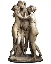 Trois figurines d'apparence grecque à-moitié dénudées et enlacées, visages rapprochés et bras embrassant les épaules.