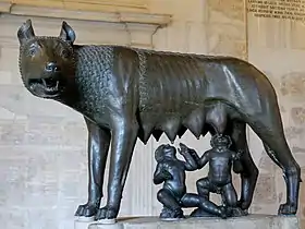 Statue en bronze d'une louve avec deux enfants en dessous qui la têtent.