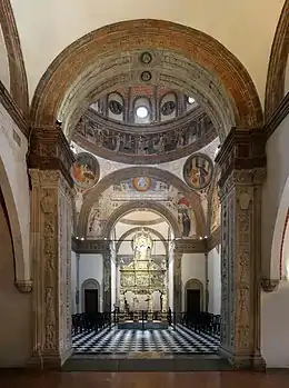 Image photographique montrant une salle carrée dotée de trois grands arcs successifs, avec une petite abside, couverte d'une coupole à seize ogives peinte à fresque. Le pavement est a damier noir et blanc et au fond un autel est encadré par deux petites portes au sommet arrondi.