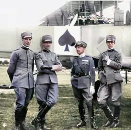 Quatre hommes en uniformes gris posant devant le fuselage d'un avion. Photo originale en noir et blanc colorisée.