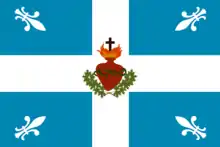 Photo du drapeau à la croix blanche sur fond bleu et chargé du dessin du Sacré-Coeur. Quatre fleurs de lys blanches figurent dans les angles du drapeau.