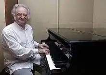 Homme souriant aux cheveux blancs, posant au piano